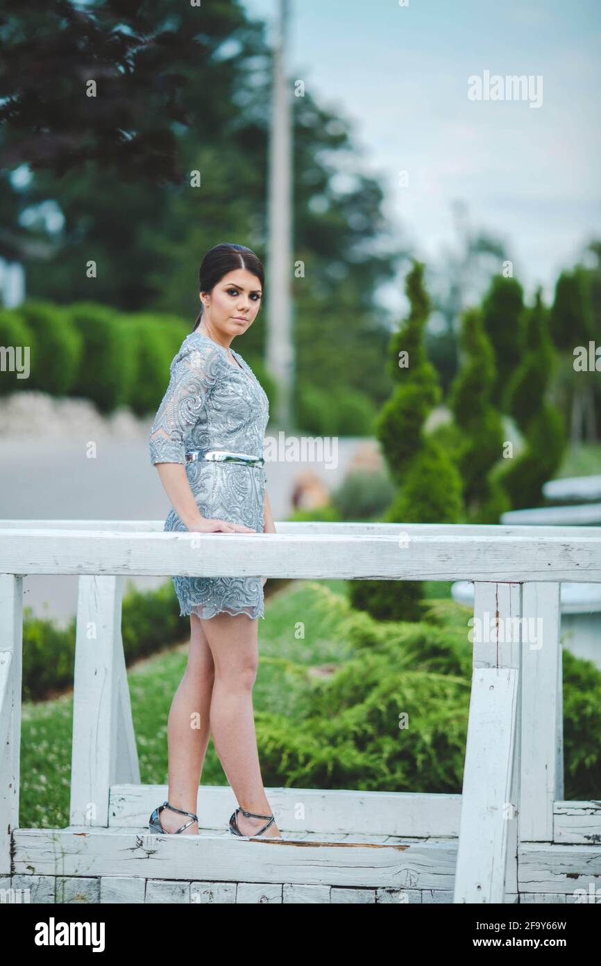 Vertikale Aufnahme einer schönen europäischen Frau in einem Mini Kleid posiert auf einer hölzernen Gartenbrücke Stockfoto