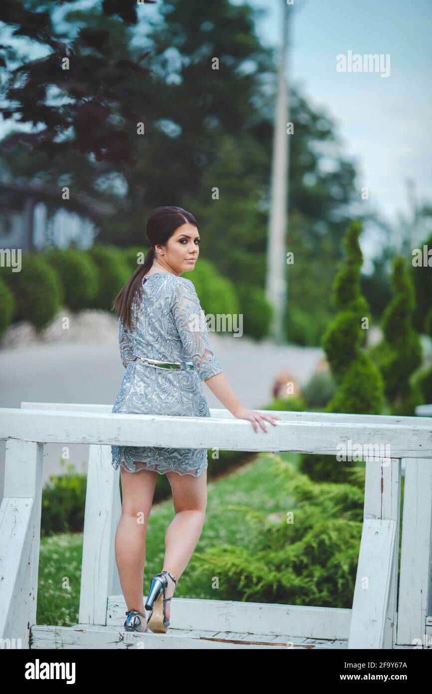 Vertikale Aufnahme einer schönen europäischen Frau in einem Mini Kleid posiert auf einer hölzernen Gartenbrücke Stockfoto