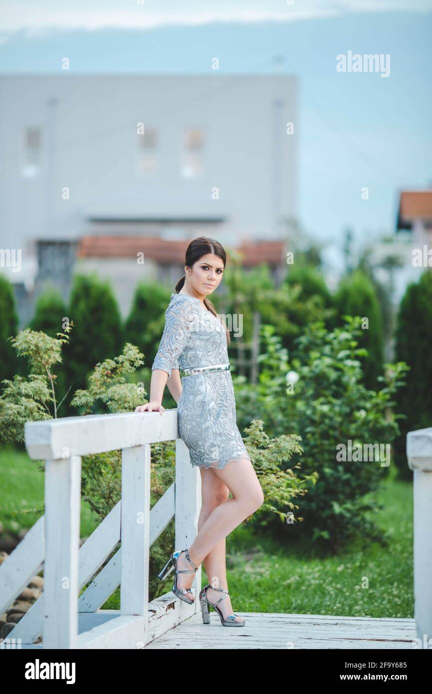 Vertikale Aufnahme einer schönen europäischen Frau in einem Mini Kleid posiert auf einem Holzgarten bri Stockfoto