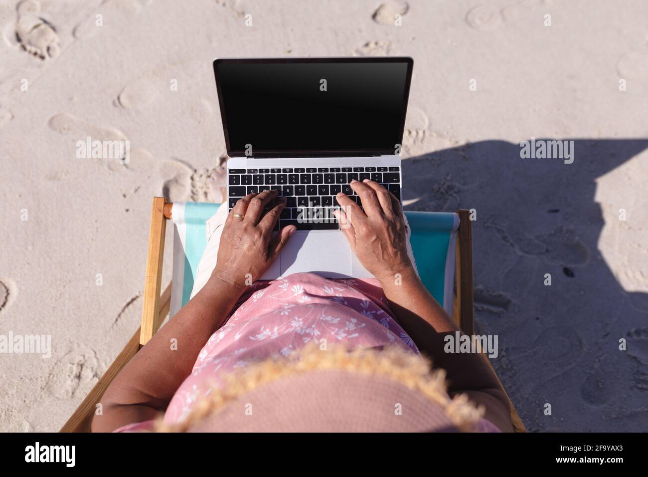 Overhead-Ansicht einer älteren afroamerikanischen Frau, die während des Aufenthalts einen Laptop verwendete Sitzen auf dem Liegestuhl am Strand Stockfoto