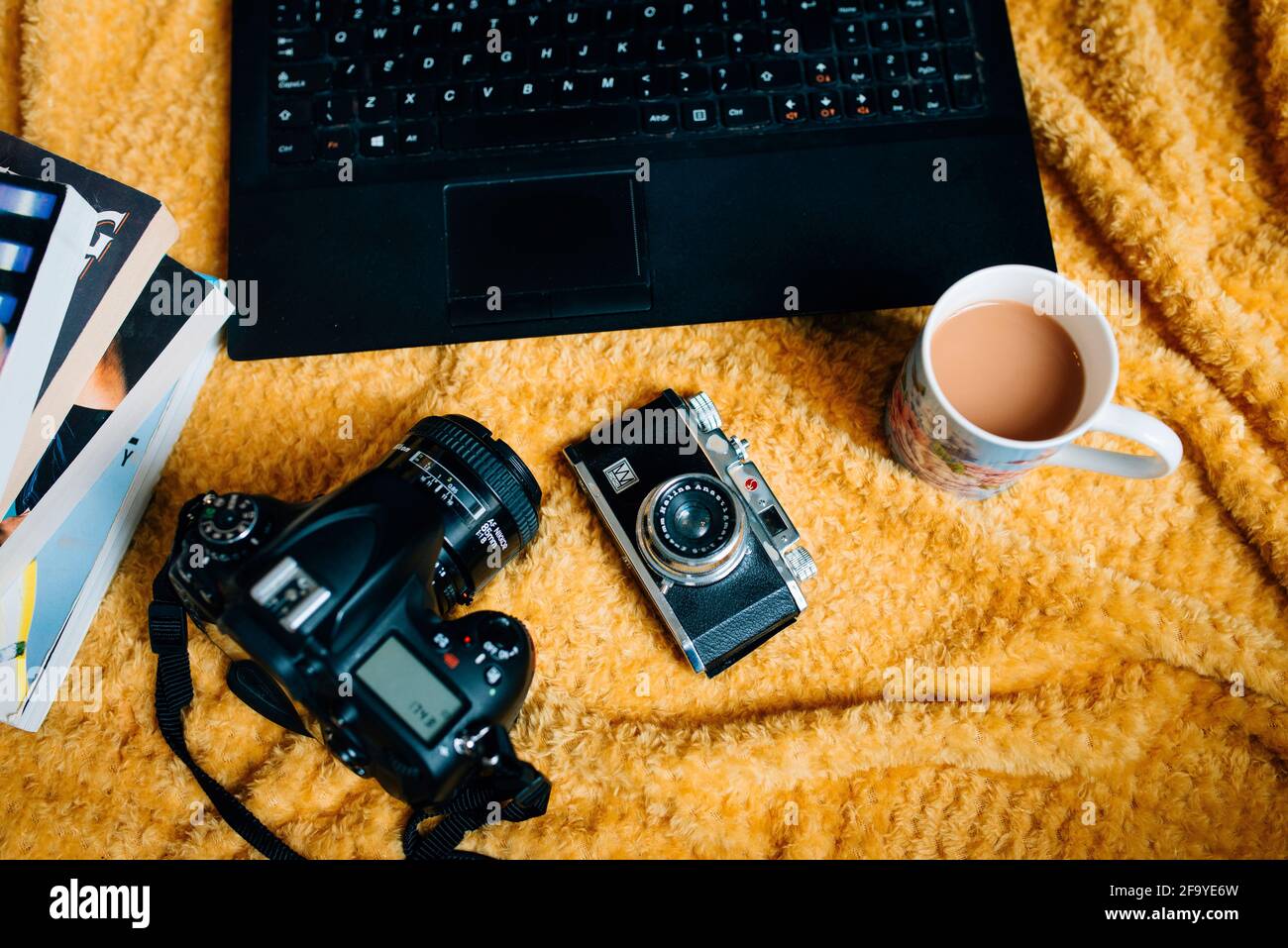 Eine flache Stillleben-Szene zu Hause mit einer Anordnung von Vintage-Kamera, DSLR, Laptop und Tasse Tee auf einer Decke. Das Leben eines kreativen Freiberuflers Stockfoto
