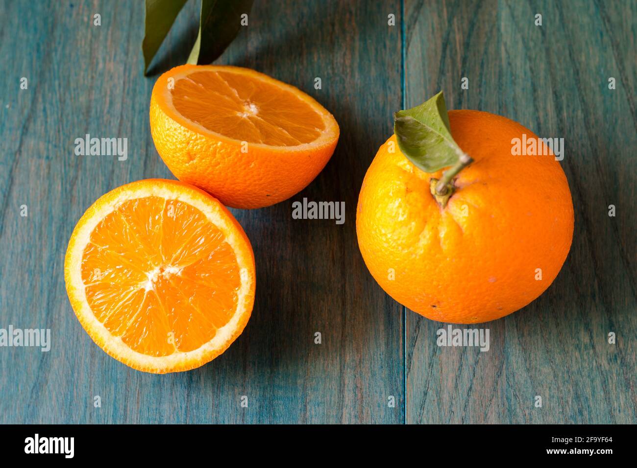 Orange in zwei Hälften geschnitten und andere Orangen auf ultramarinfarben gefärbt Holzhintergrund Stockfoto