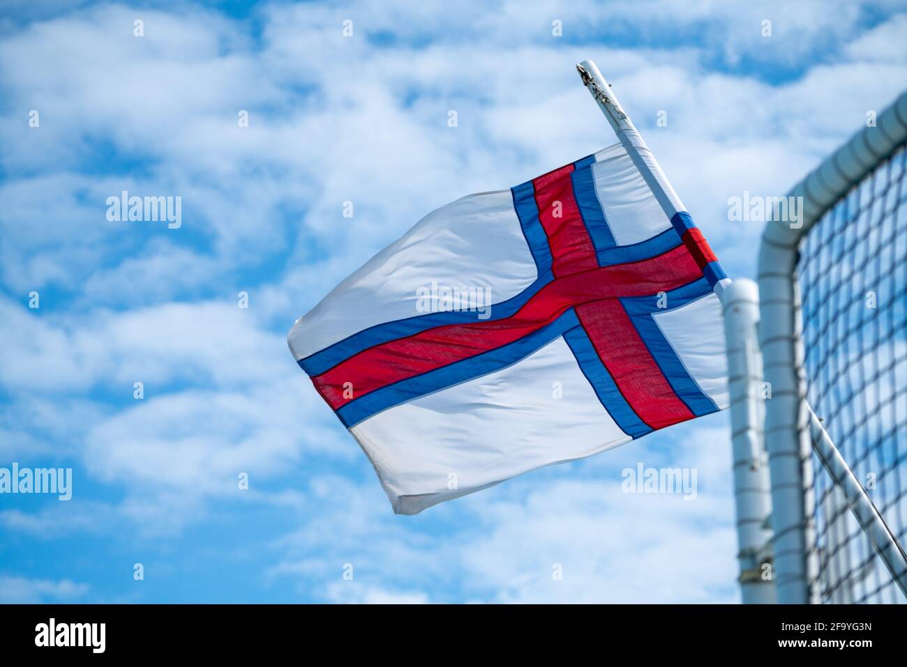 Die färöische Nationalflagge winkt bei starkem Wind mit blauem und bewölktem Himmel im Hintergrund. Stockfoto