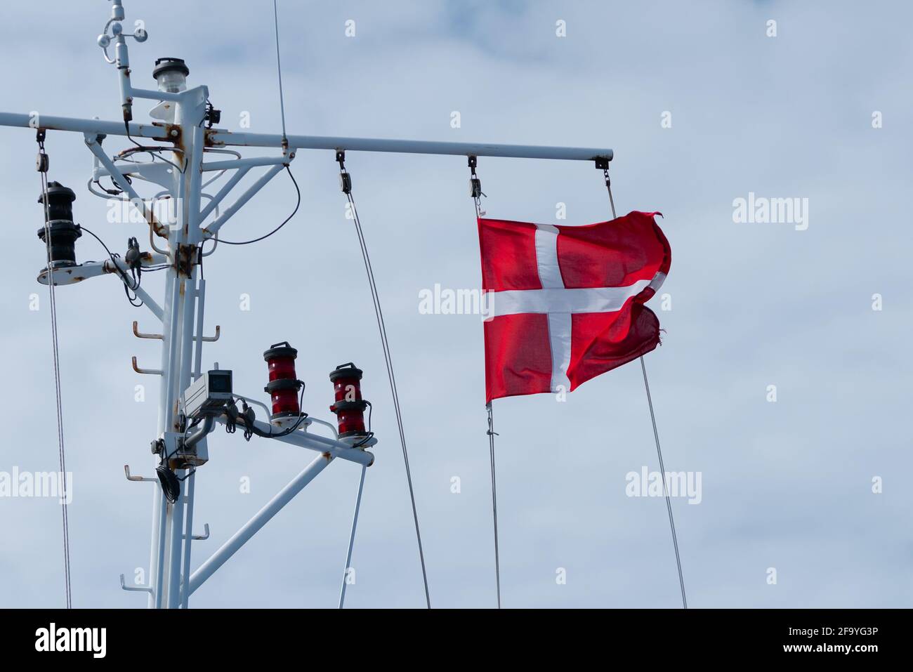 Dänische Flagge winkt im Wind mit bewölktem Himmel im Hintergrund. Am Fahnendraht auf einem Kreuzschiff befestigt. Stockfoto