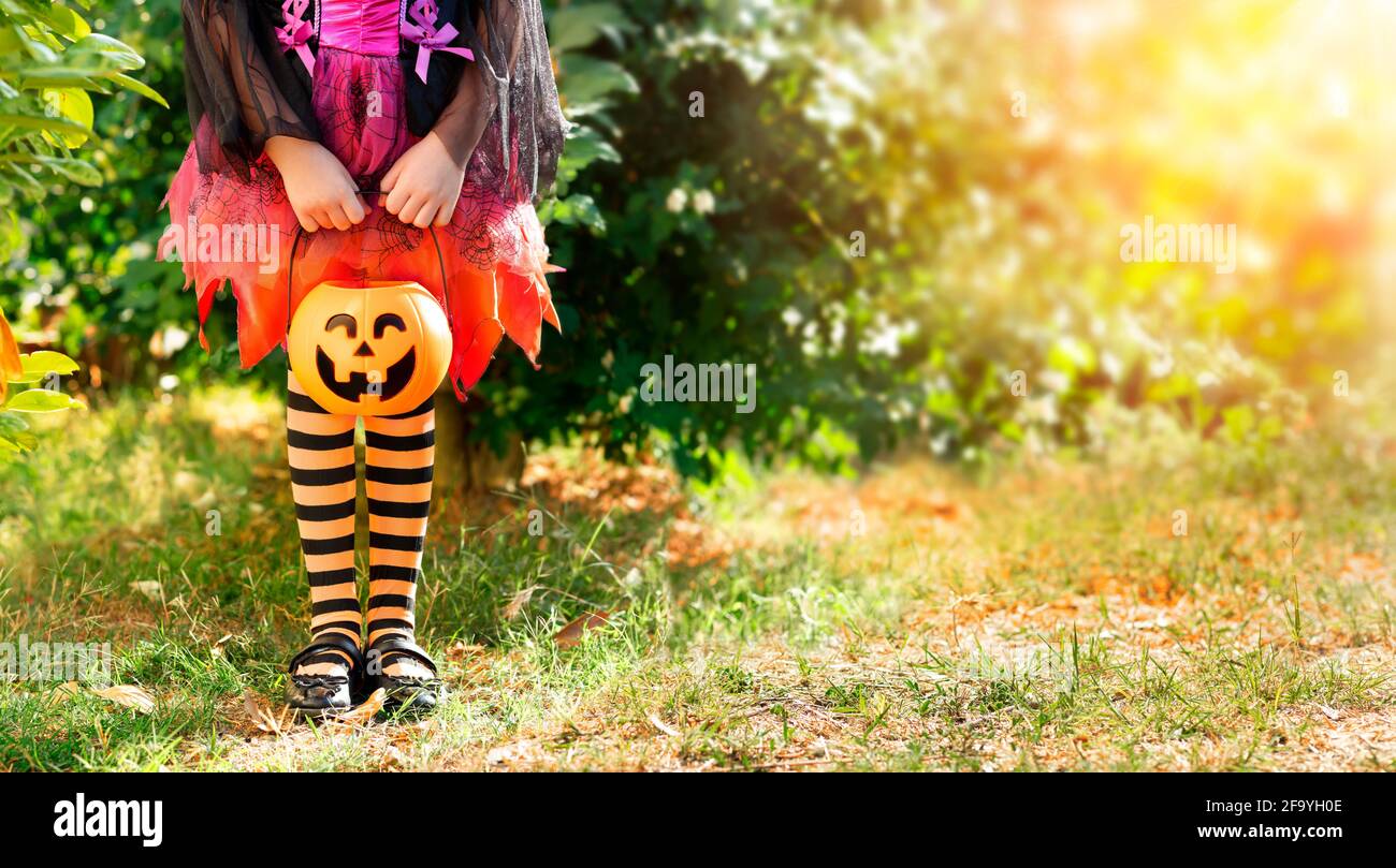 Kleines Mädchen mit Süßigkeitenkorb auf Wiese - Halloween Trick Oder Behandeln Sie Das Konzept Stockfoto