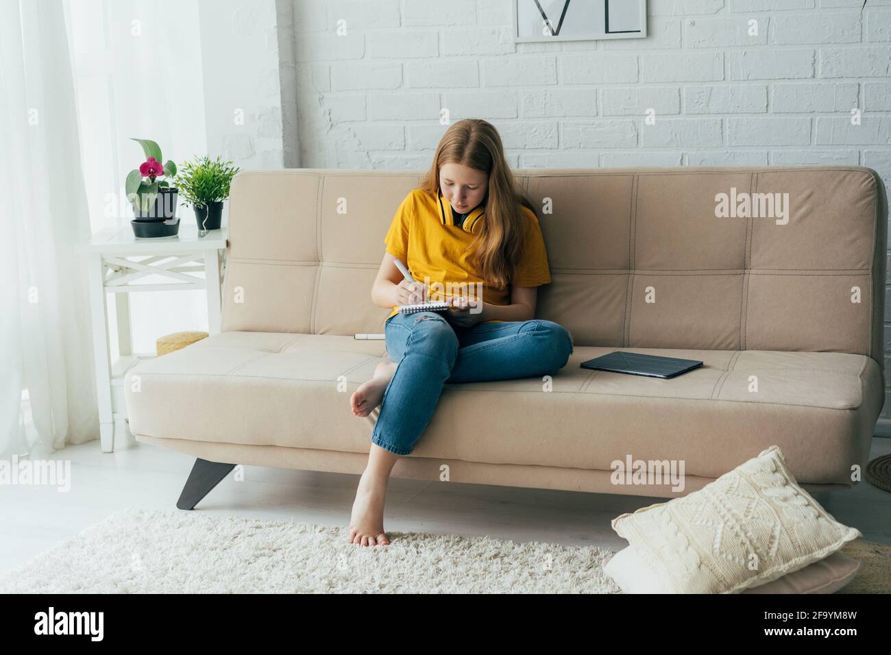 Mädchen Schulmädchen Teenager sitzt auf der Couch zeichnet eine Skizze in ein Notizbuch. Stockfoto