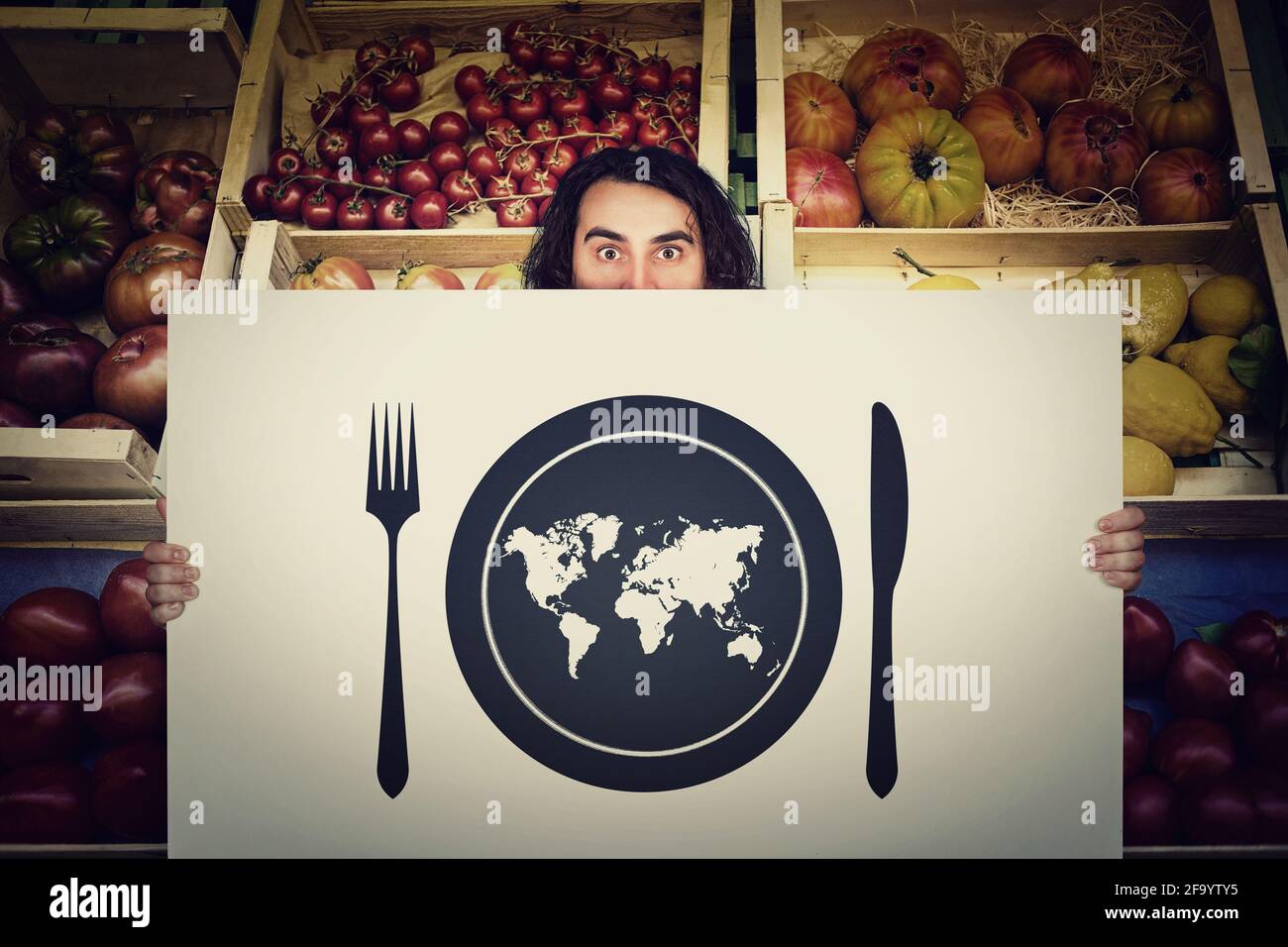 Globaler Hunger, Nahrungsmittelversorgung. Schockierter Mann, der ein Warnsignal vor einem Lebensmittelgeschäft hält. Weltkarte in einem Teller mit Messer und Gabel. Stockfoto
