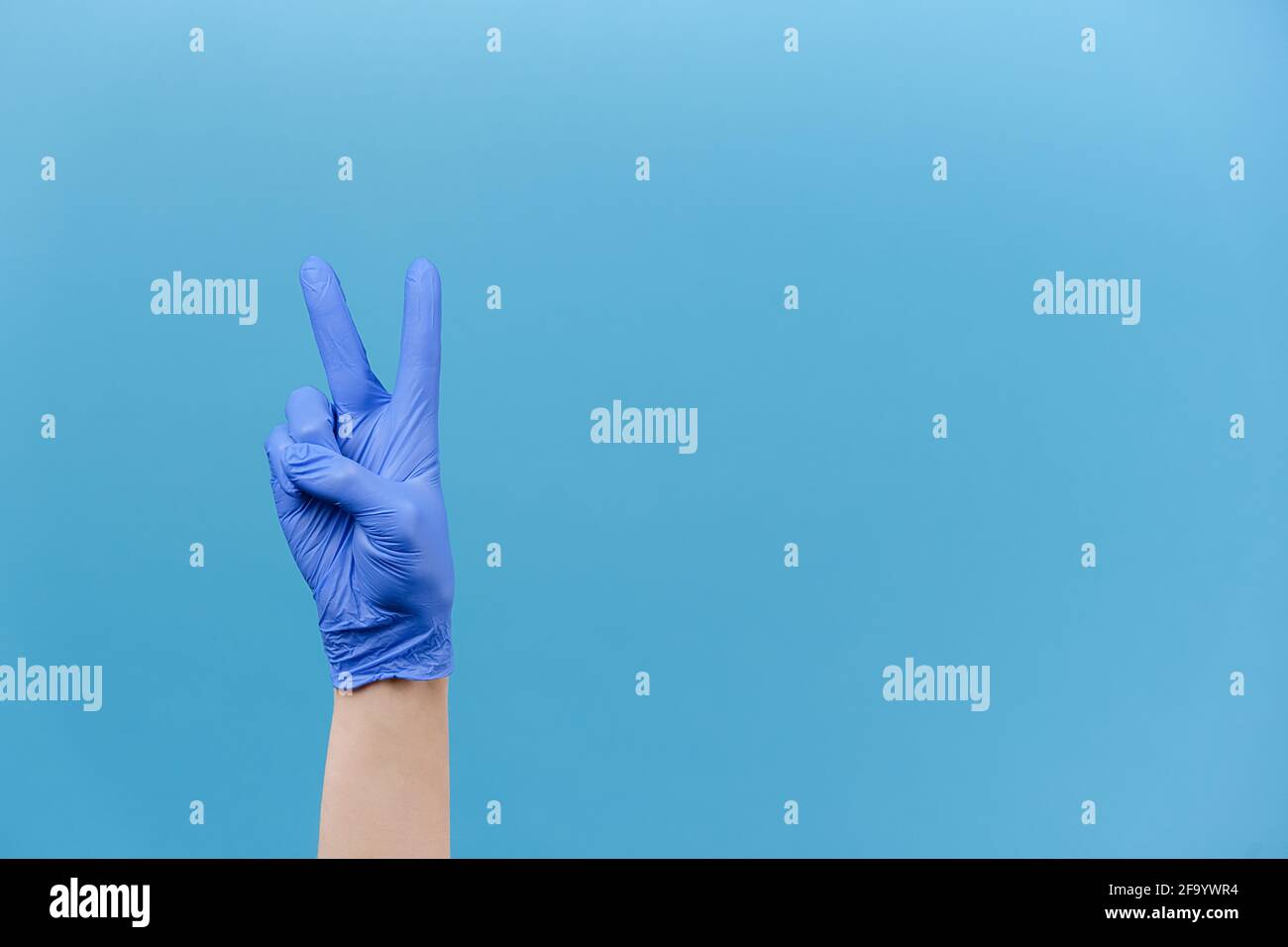 Nahaufnahme der männlichen Hand in medizinischen Schutzhandschuhen zeigt zwei Finger nach oben, isoliert in blauen Studio-Hintergrund mit Kopieplatz, drückt Feier Stockfoto