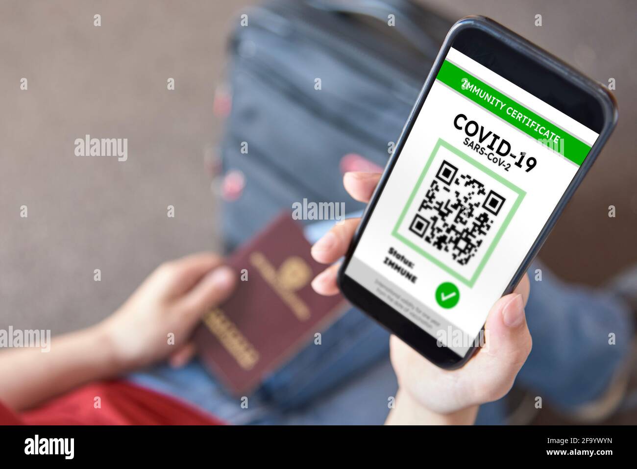 Nicht erkennbare junge Frau, die unterwegs ist und ein Smartphone mit einer Immunitätsbescheinigung gegen Covid19 in der Hand hat. In der anderen Hand hält sie einen Passor Stockfoto