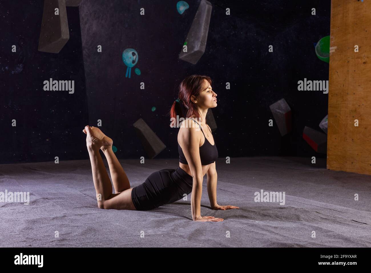 Eine athletische junge Frau, die in der Kletterhalle Yoga praktiziert und sich vor dem Bouldern aufwärmt Stockfoto