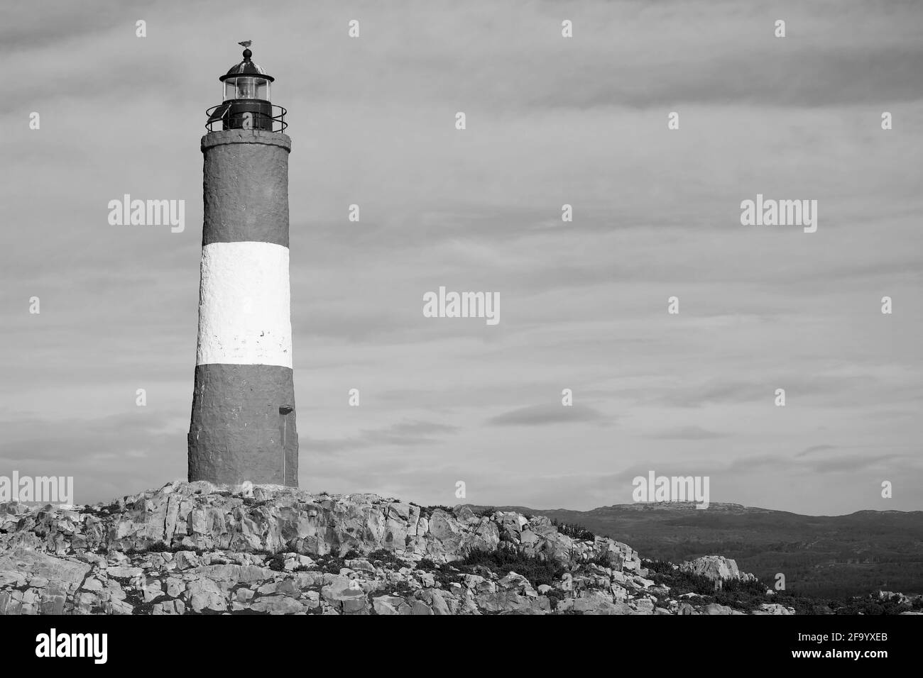 Leuchtturm auf einer felsigen Insel gegen bewölkten Himmel in monochromen Stockfoto