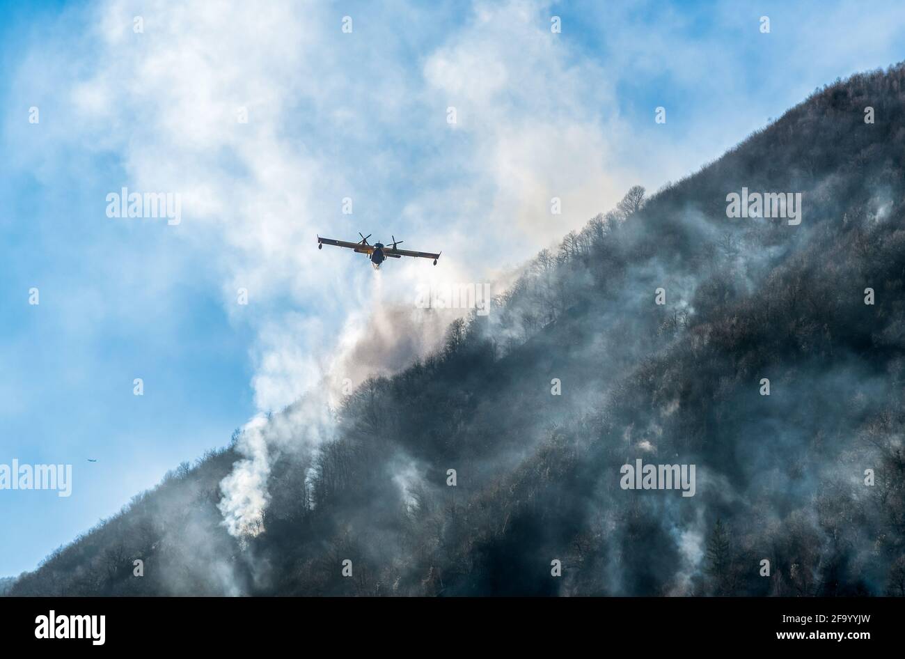 Löschflugzeuge, die das Wasser fallen lassen, um einen Brand auf einem Berg über dem Ghirla-See in Valganna, Provinz Varese, Italien, zu bekämpfen Stockfoto