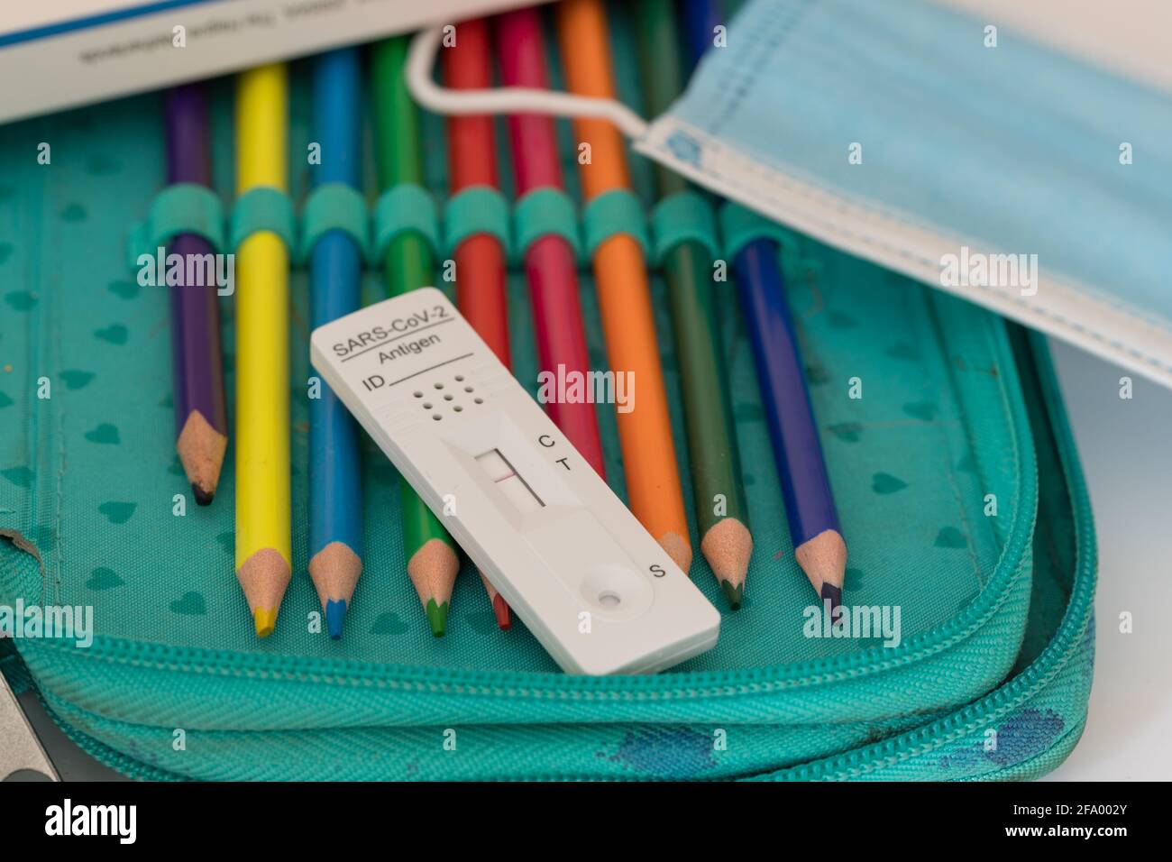 Operationsmaske und Corona SARS-CoV-2 Antigen-Test mit negativem Ergebnis auf farbigem Bleistift in einem Federmäppchen, Fokus auf Vordergrund Stockfoto