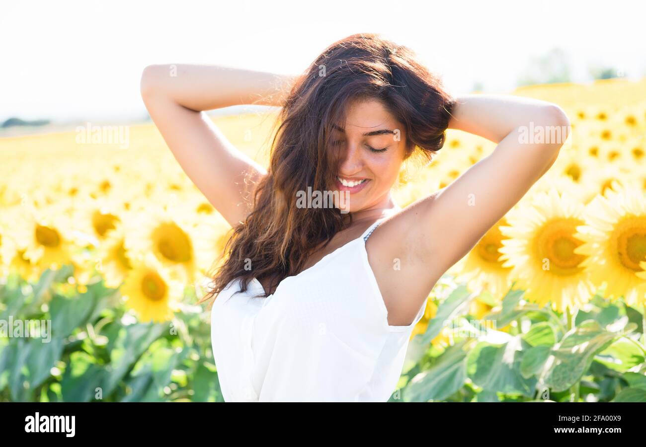 Ein schönes lächelndes Mädchen unter den Sonnenblumen. Motiv mit unscharfem Hintergrund, perfekte Aufnahme für Urlaub, Frühling und Landleben. Stockfoto