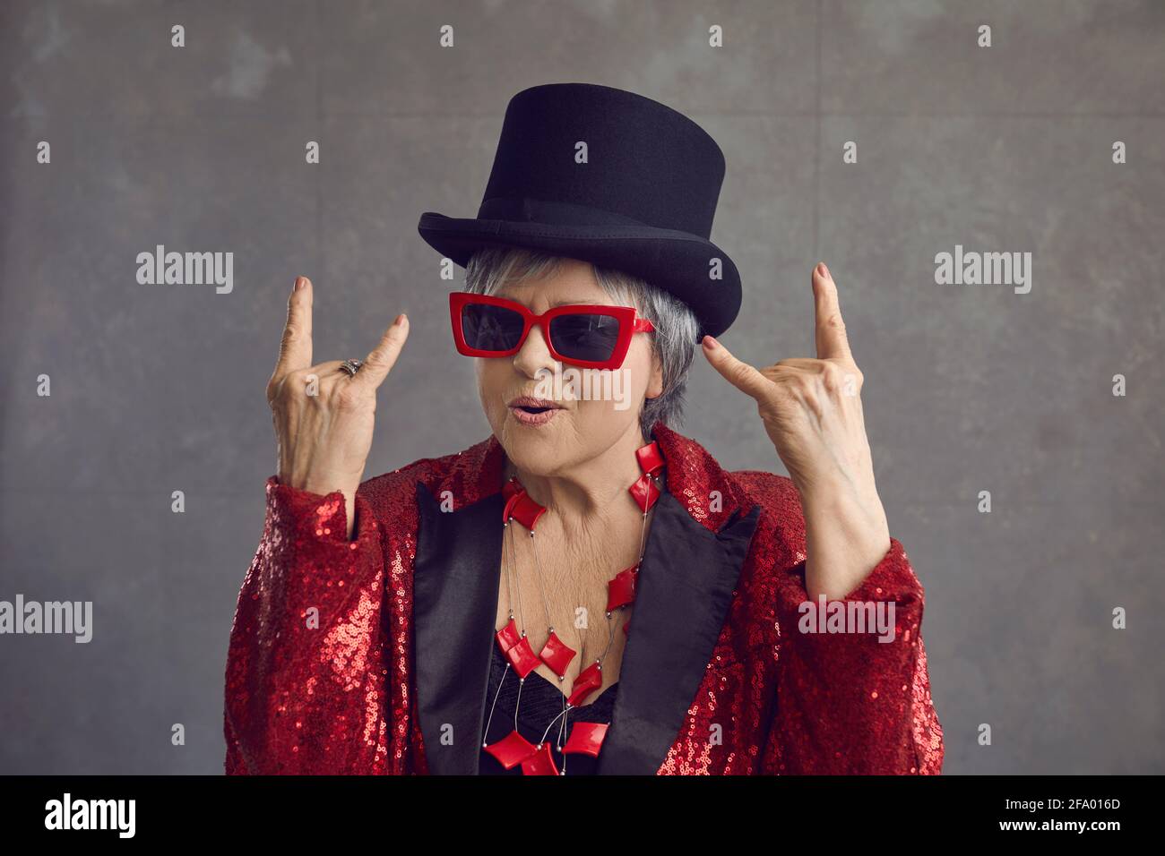 Lustige verrückte ältere grauhaarige Dame mit Zylinderhut, die Rock'n'Roll zeigt Handzeichen Stockfoto