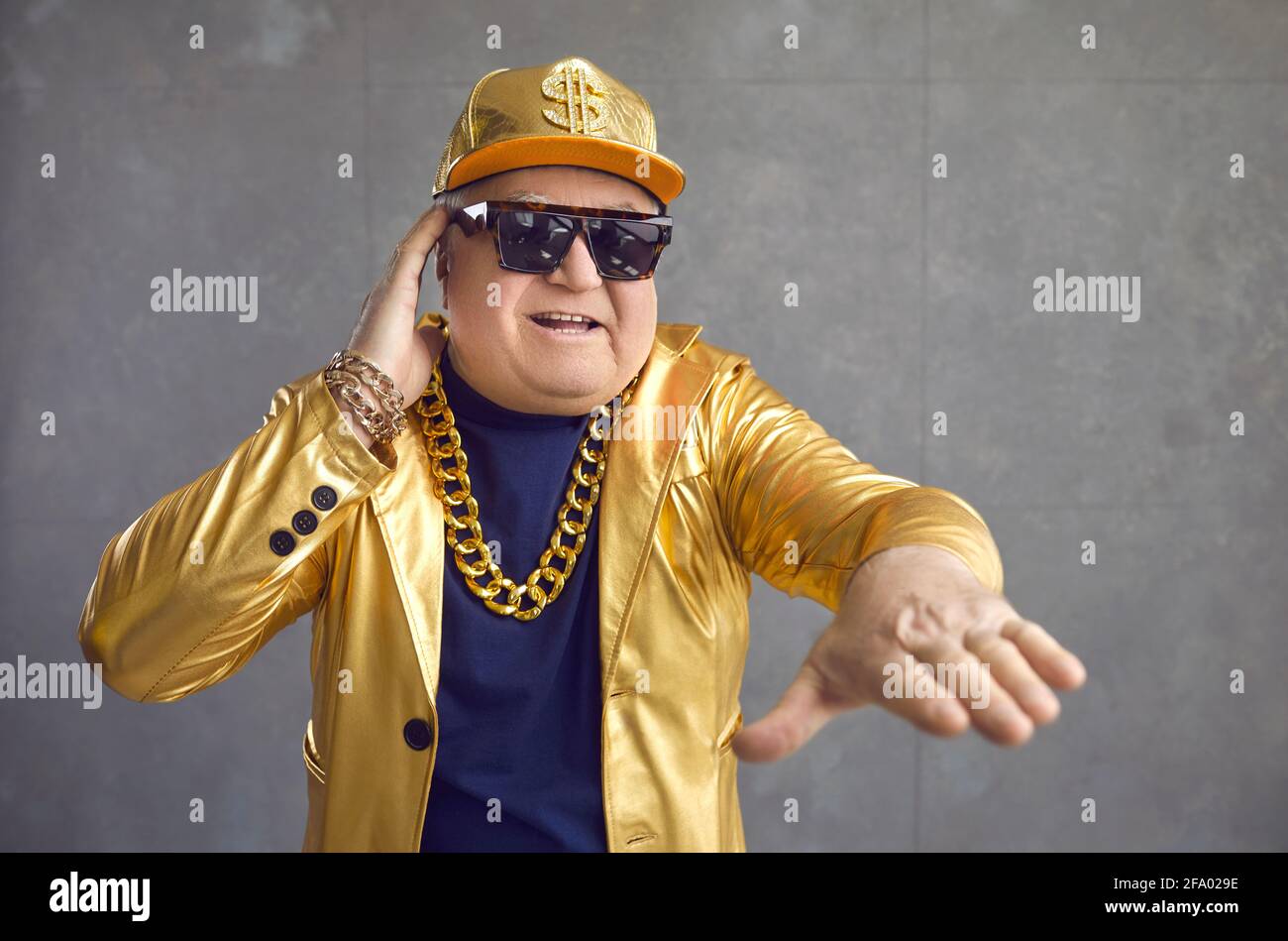Lustiger älterer Mann in goldener Jacke, Baseballmütze und Kette, der Musik auf der Disco-Party spielt Stockfoto