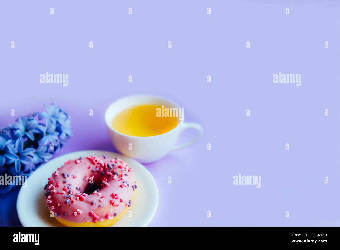 Rosa, zuckerglasierte Donut, Tasse Tee und Hyazinthen-Blume auf buntem Hintergrund. Stockfoto