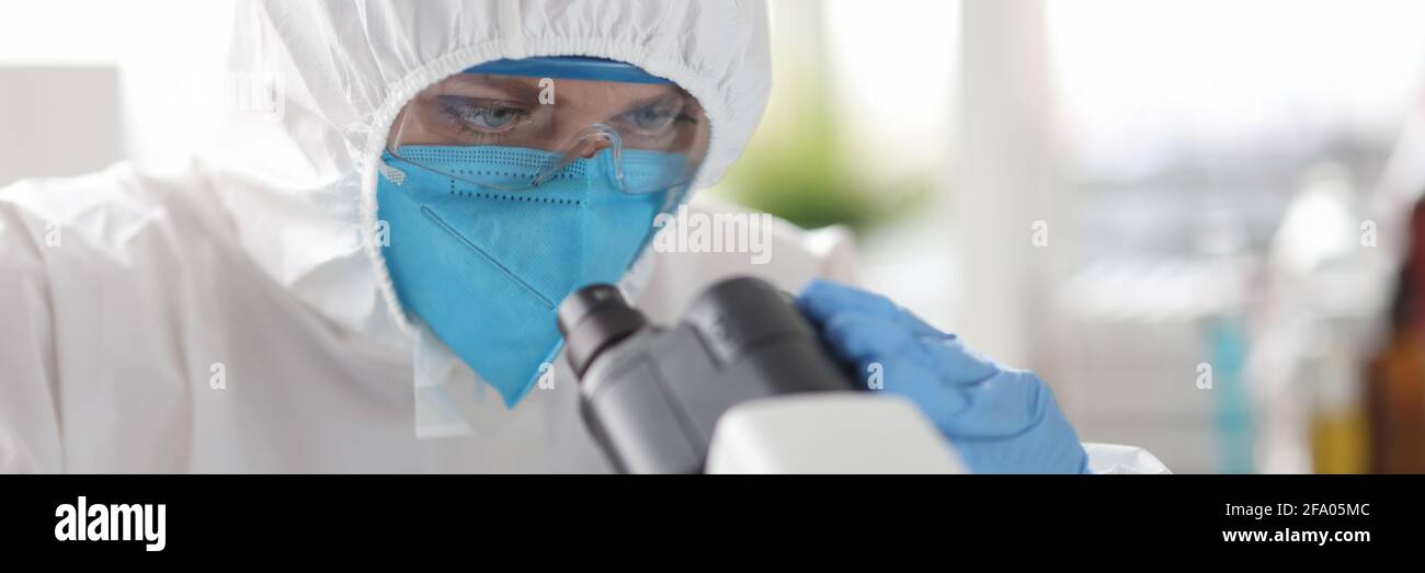 Wissenschaftler in Schutzanzug und Atemschutzmaske Blick durch Mikroskop in Labor Stockfoto