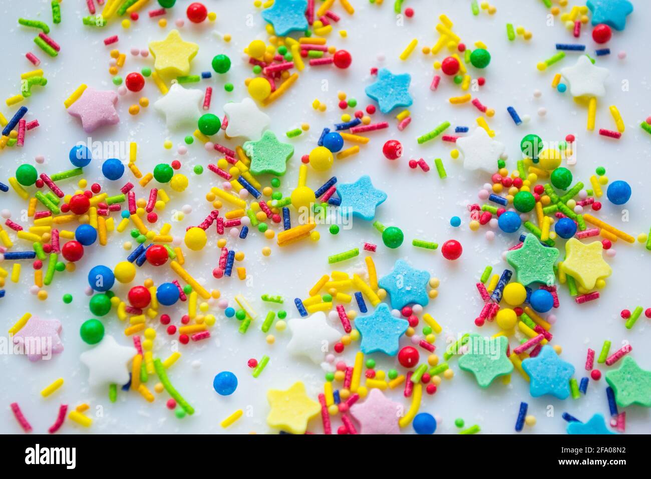 Mehrfarbiger festlicher Hintergrund einer Streuung von Zuckerzuckerstreuseln für Cupcakes und andere Backwaren in Form von Sternen, Stöcken und Kugeln. Helle Spalte Stockfoto