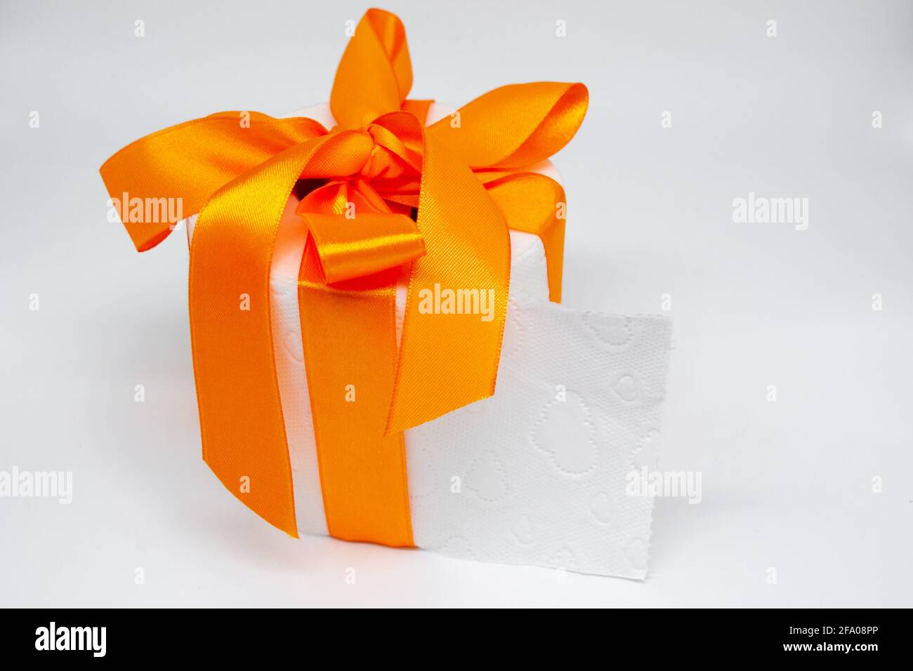 Weiße Toilettenpapierrolle mit leuchtend orangefarbenem Satinband als Geschenk gebunden. Stockfoto