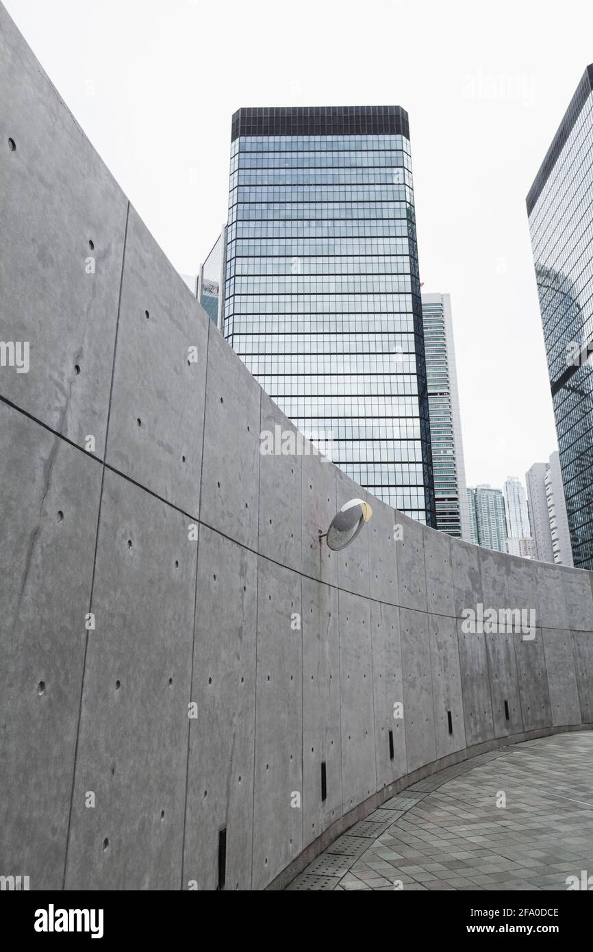 Moderner Blick auf die leere Stadtstraße mit Betonmauer und Wolkenkratzern im Hintergrund, Bürohochhäuser in Hongkong Stockfoto