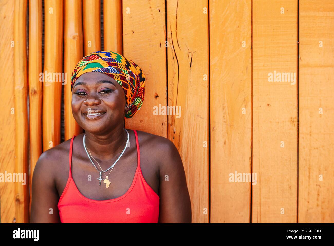 Afrikanische Frau mit einem hoffnungsvollen glücklichen Lächeln, das gegen eine steht Bemalte Holzwand im tropischen Dorf Keta Ghana Westafrika Stockfoto