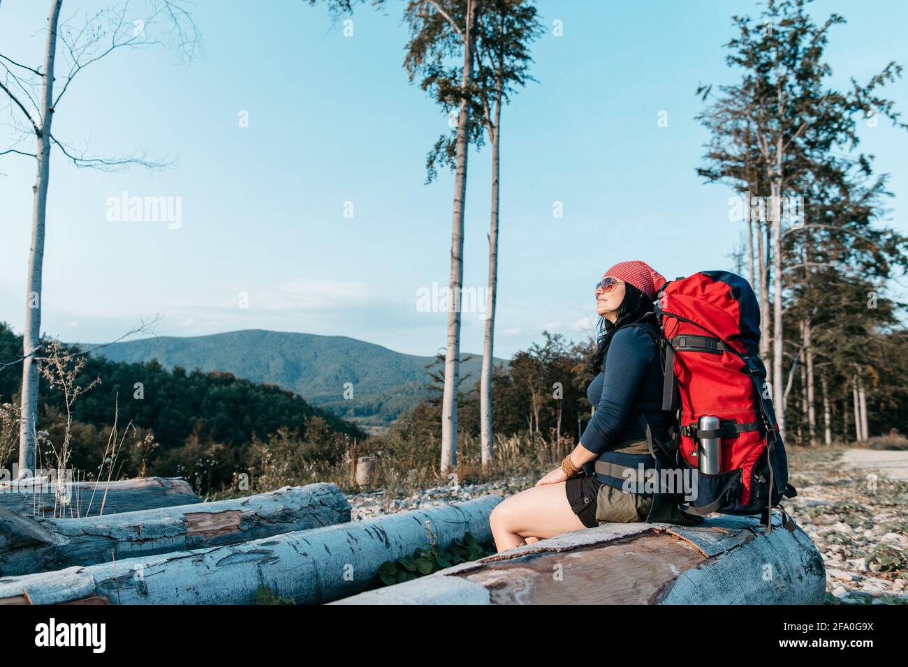 Eine Wanderin, die sich ausruhte und den Sonnenuntergang genoss. Ein Porträt einer Frau mit Rucksack, die eine Pause einnimmt und die Aussicht bewundert. Stockfoto