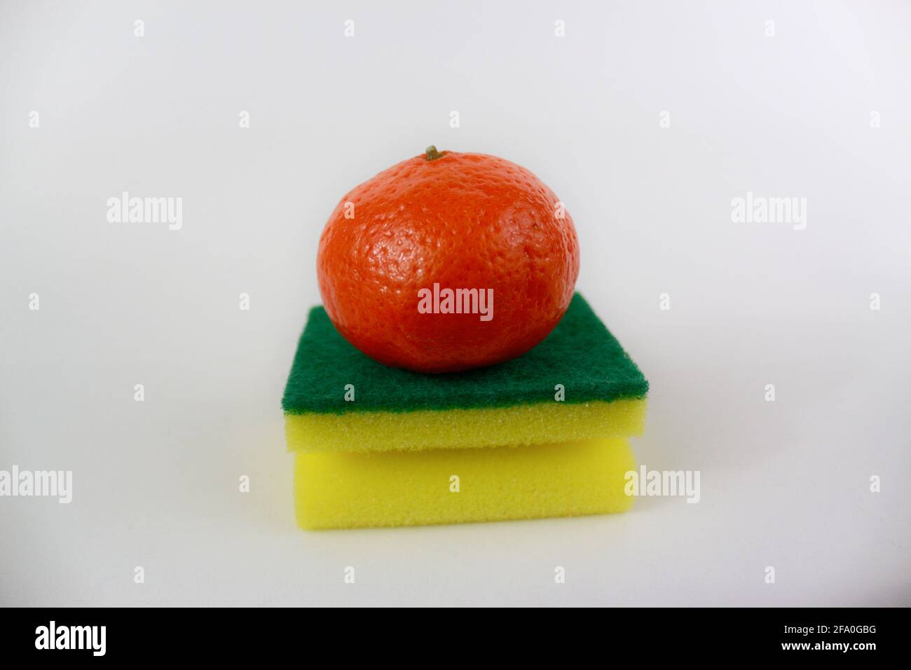 Eine Mandarine auf einem gelbgrünen Schwamm der Küche isoliert Weißer Hintergrund Stockfoto