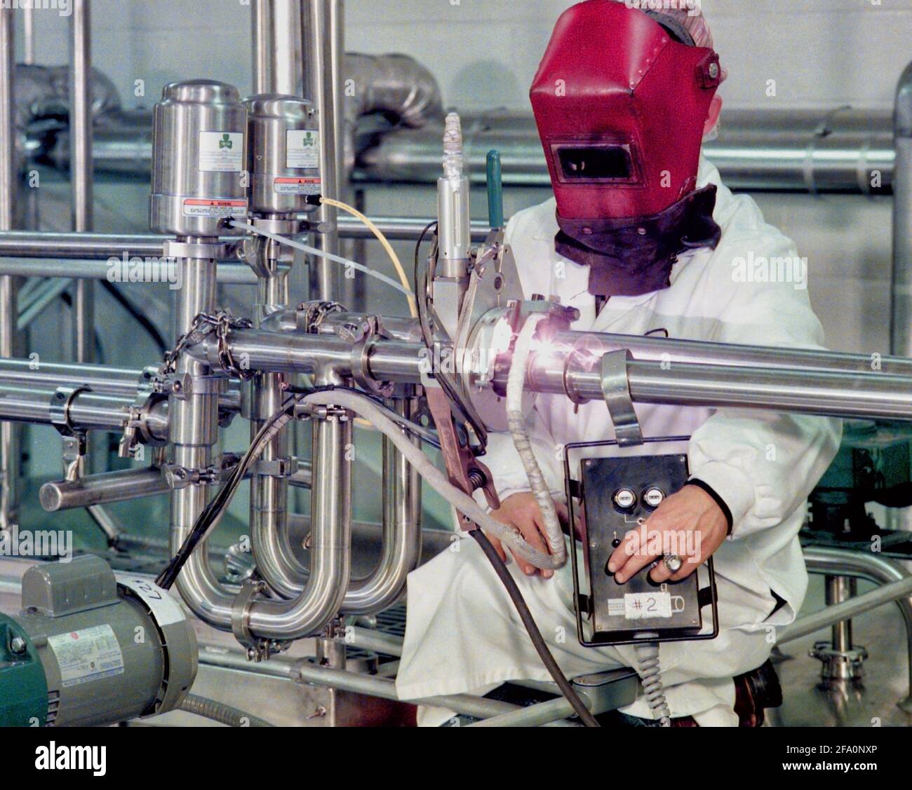 Ein Schweißer verwendet einen Orbitalschweißroboter, um Edelstahlrohre in einer lebensmittelverarbeitende Einrichtung miteinander zu schweißen. Stockfoto