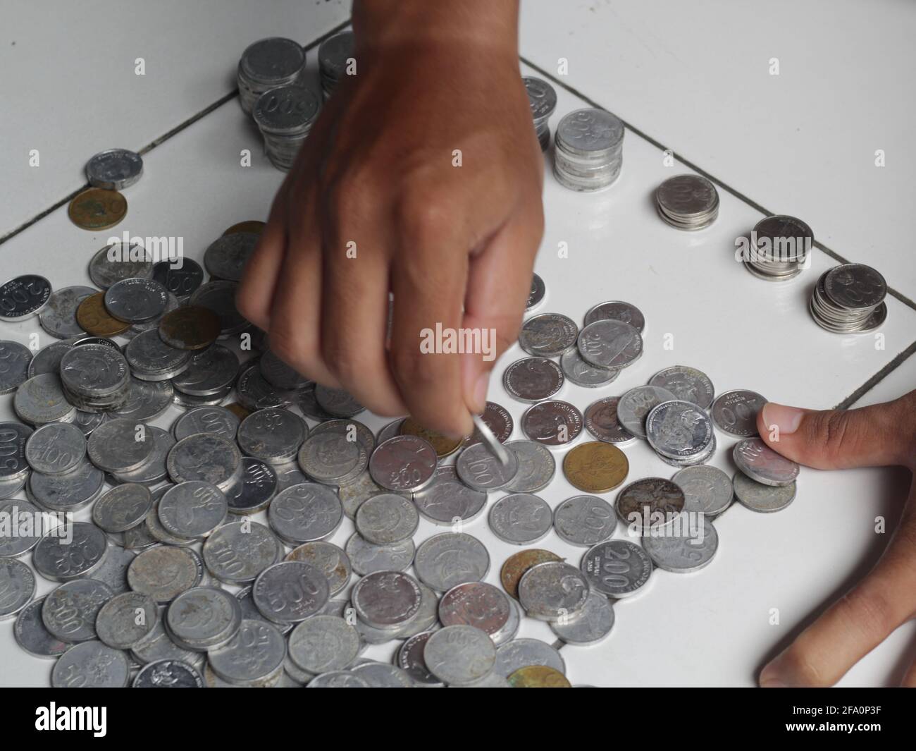 Mann, der indonesischen Penny zählt. Gestapelte Rupiah-Münze. Stockfoto