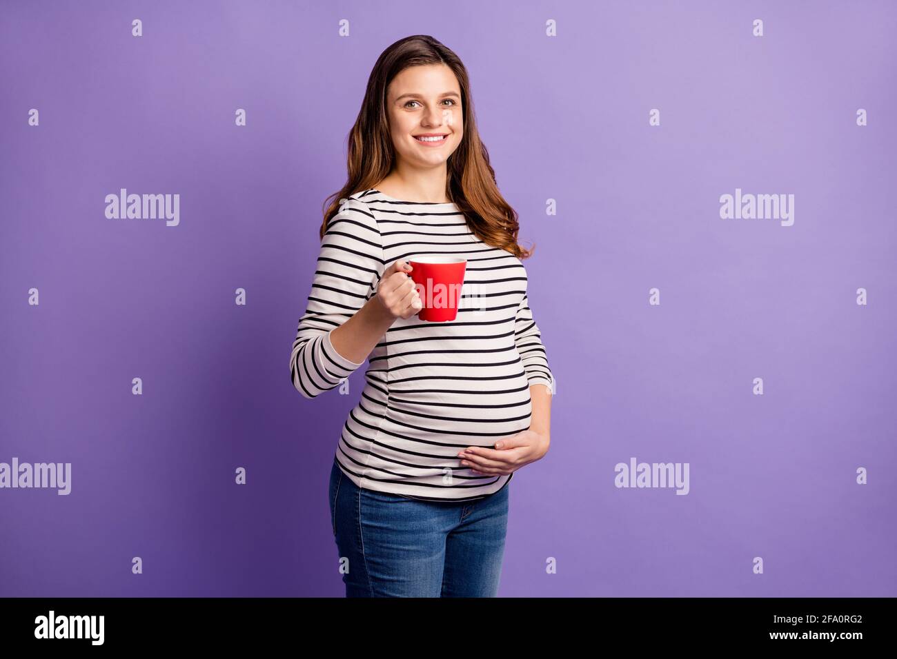 Foto von Schwangere Dame halten Tasse trinken Tee Handbauch Tragen gestreiftes Hemd isoliert violetten Hintergrund Stockfoto