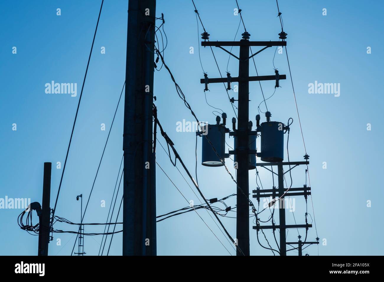 Reihe von verketteten Strommasten mit elektrischen Übertragungsleitungen und Transformatoren bei Sonnenaufgang Stockfoto