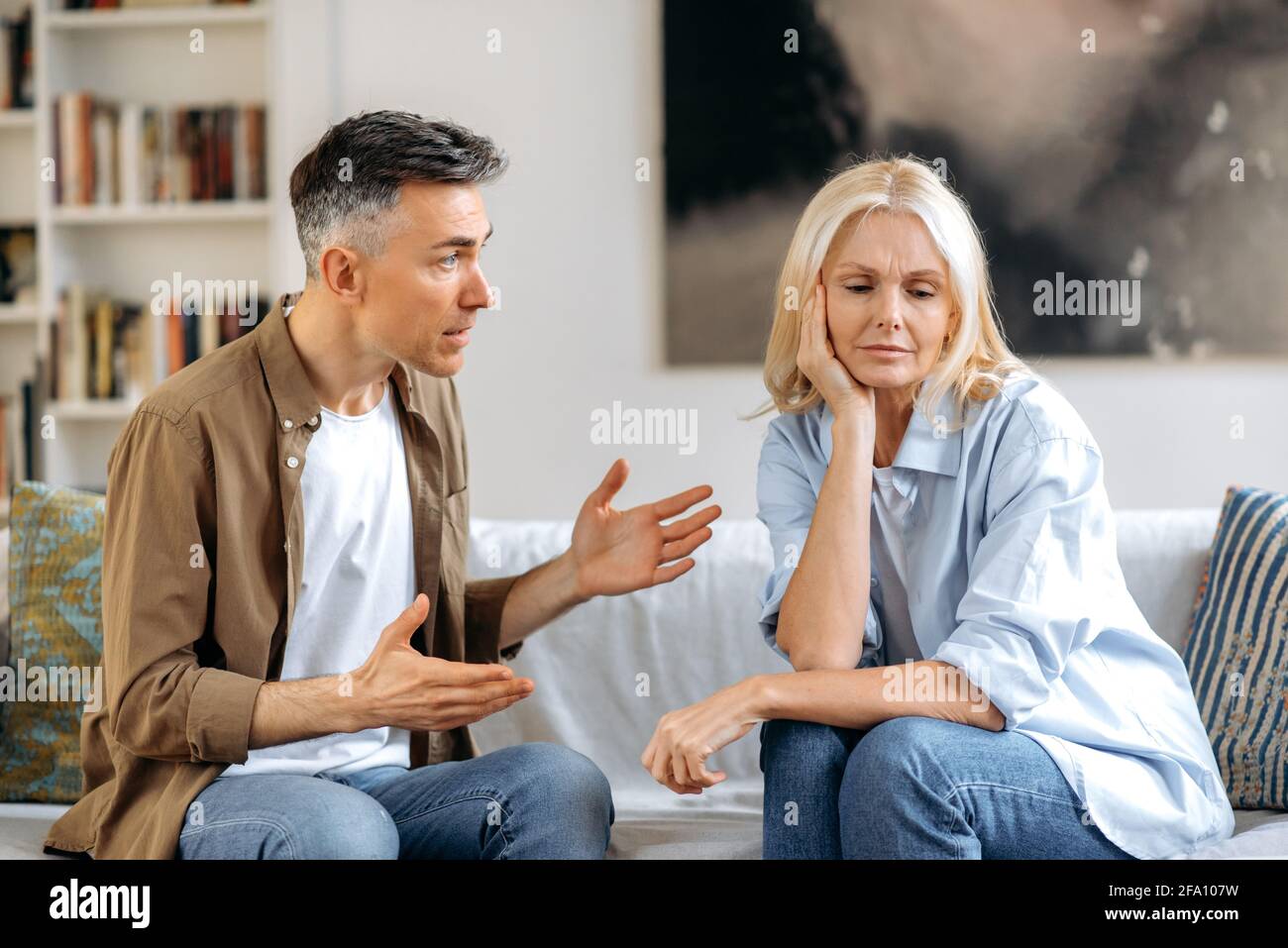 Emotionaler Dialog eines Ehepaares im Wohnzimmer auf der Couch. Empört besorgt Ehemann emotional drückt seine Meinung zu seiner Frau, verärgert Frau, die ihren Kopf auf ihre Hand ruhen und nach unten schauen Stockfoto