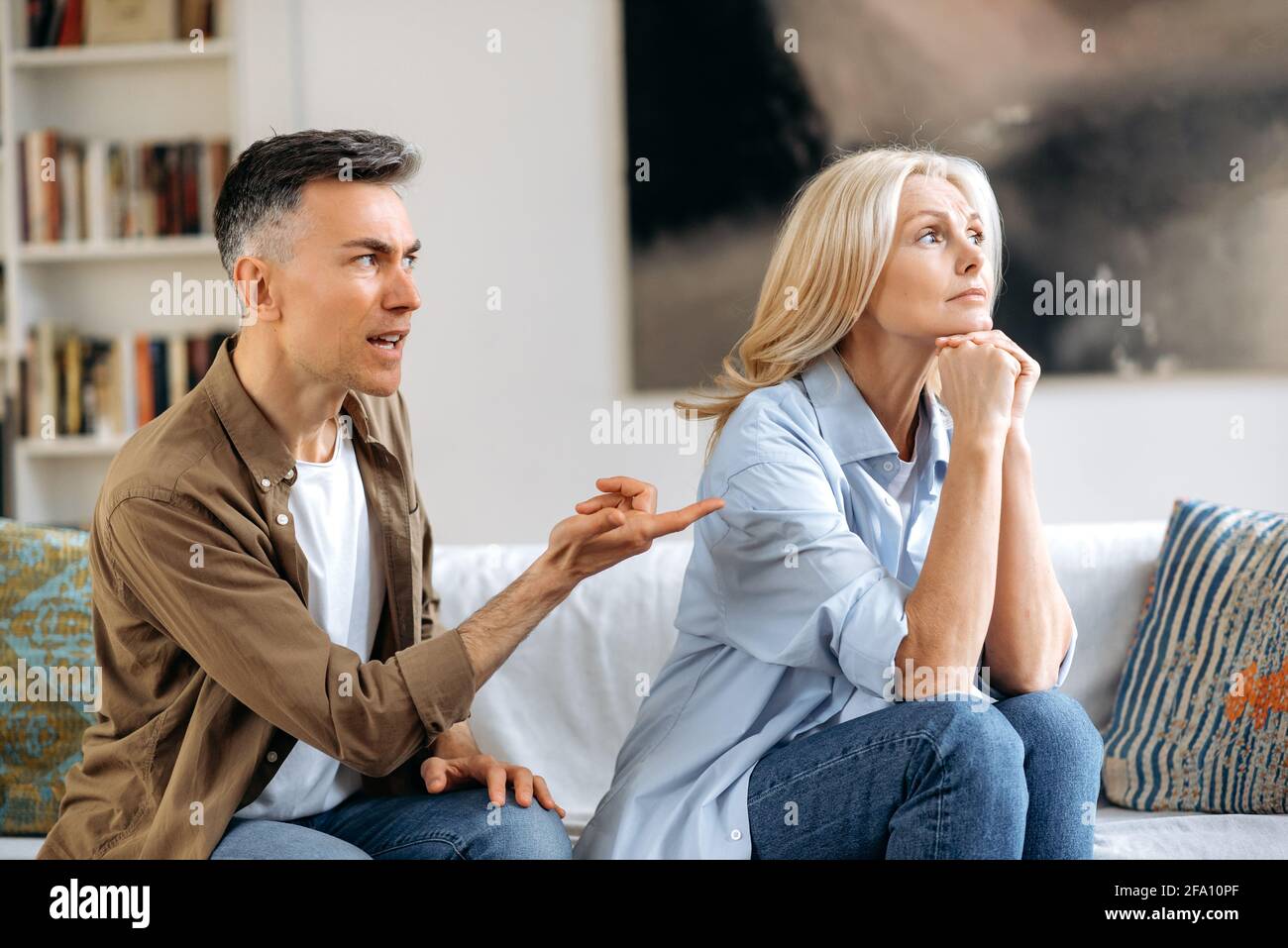Ein aufgeregter und verstörter grauhaariger Ehemann schreit und schaut seine Frau an, mit Gesten mit der Hand, kann keine Entscheidung treffen oder Kompromisse eingehen, ein Streit zwischen Ehepartnern. Missverständnis der Familie, Streit Stockfoto