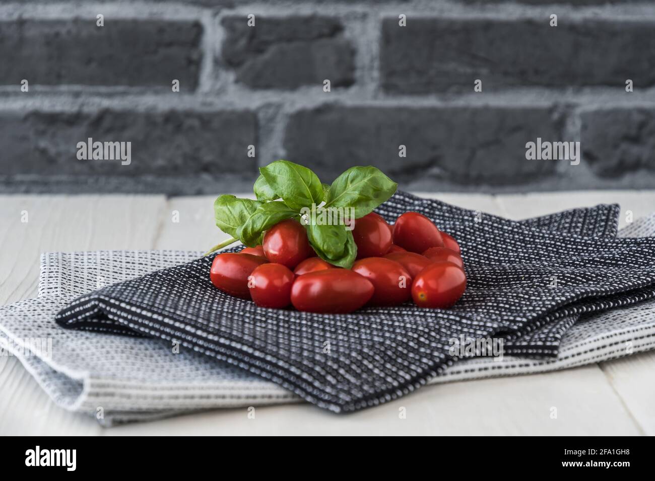 Reife Kirschtomaten mit Basilikumzweig auf schwarz-weiß Geschirrtücher vor grauem Steinhintergrund Stockfoto