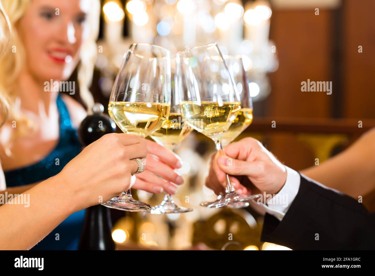 Gute Freunde - Mann und Frau, trinken Wein und klirrende Gläser in einem feinen Restaurant, jedes mit einem Glas in der Hand, ein großer Kronleuchter ist in Back Stockfoto