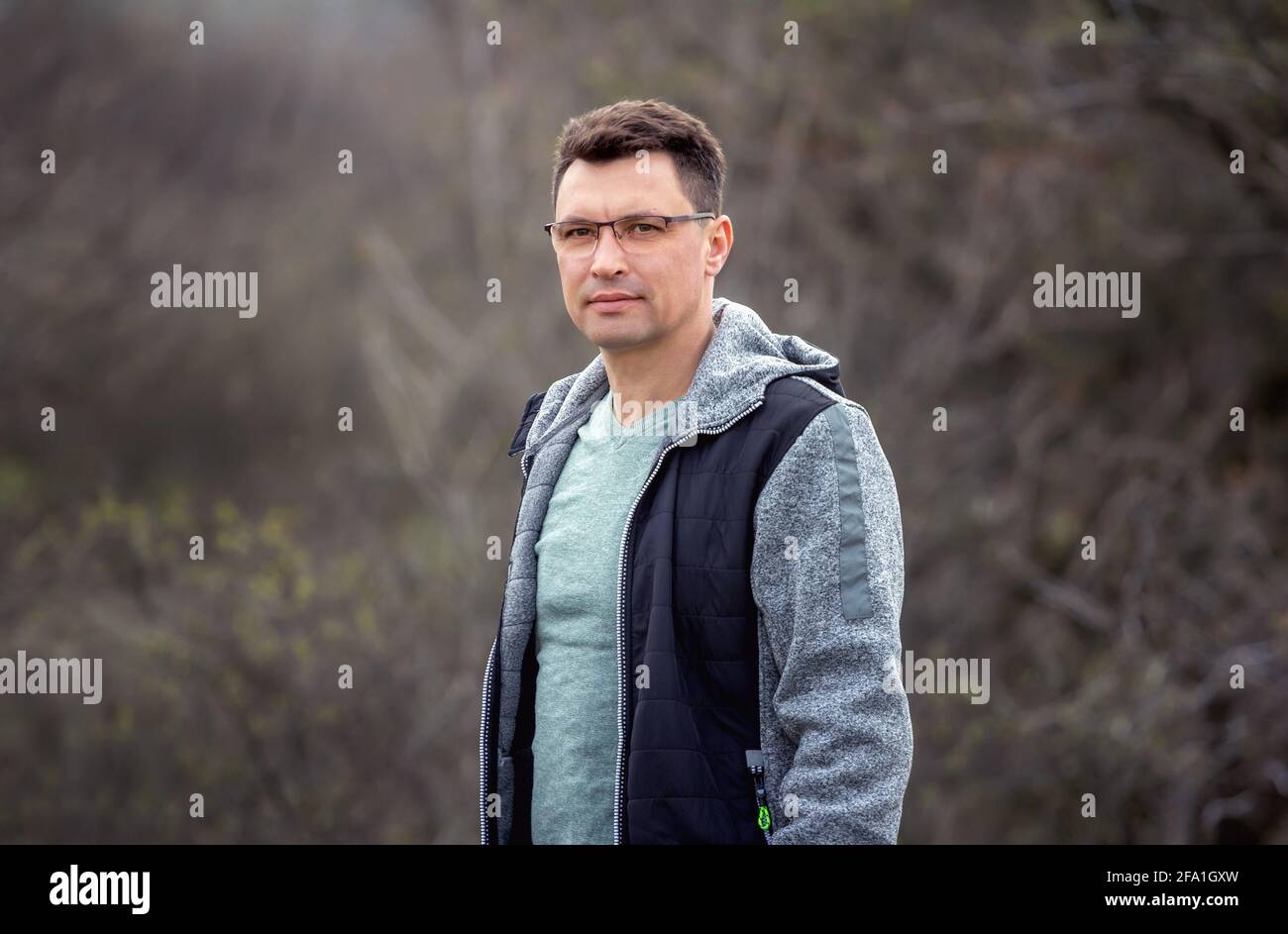 Porträt eines attraktiven Brünetten Mannes, der eine Brille trägt und seinen Spaziergang in einem Frühlingspark genießt Stockfoto