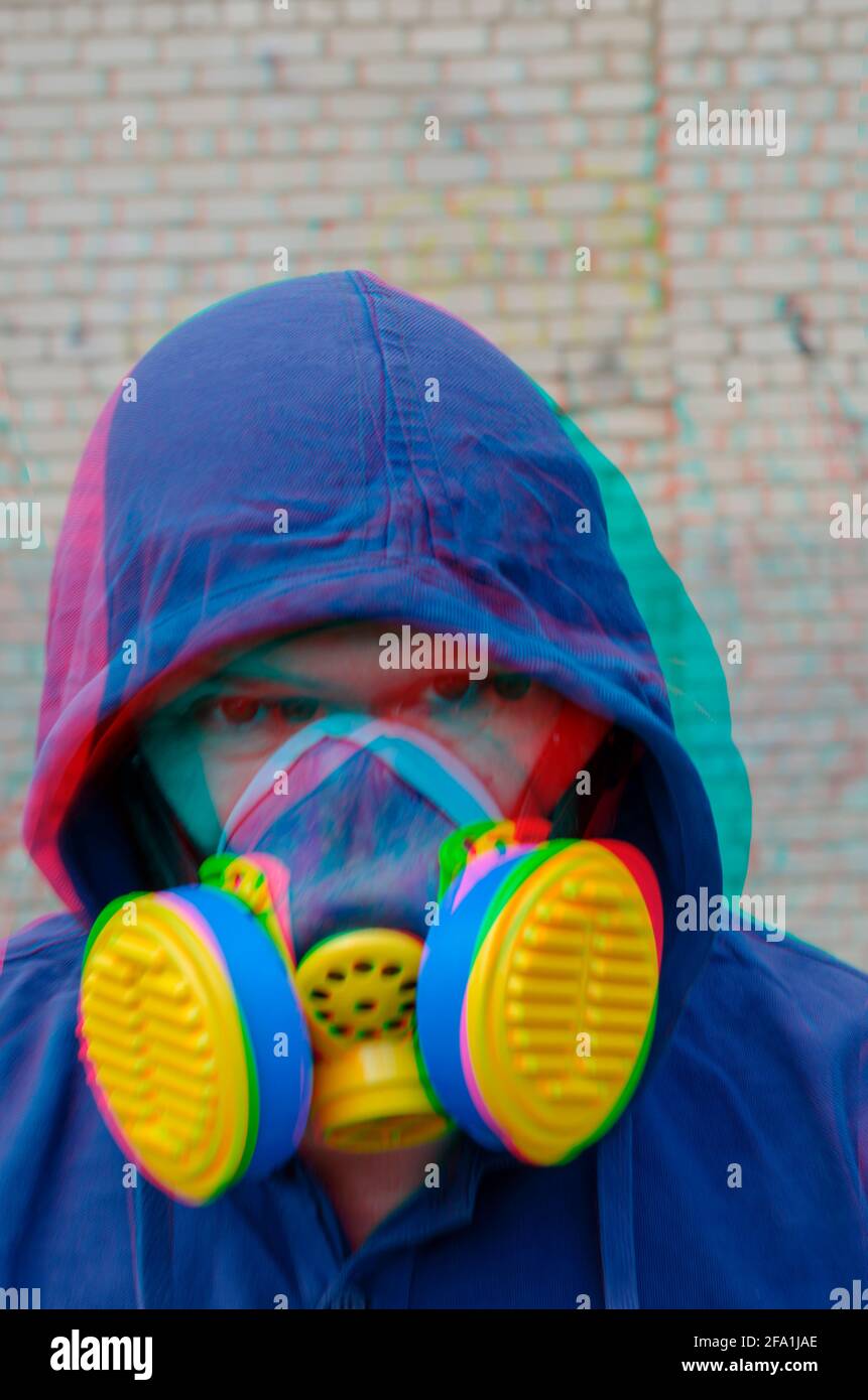 Defokussiertes Porträt eines unverkennbaren Mannes, der eine Kapuze und eine blau-gelbe Atemschutzmaske mit Split-Glitch-Effekt trägt. Ein erwachsener Mann schaut auf die c Stockfoto