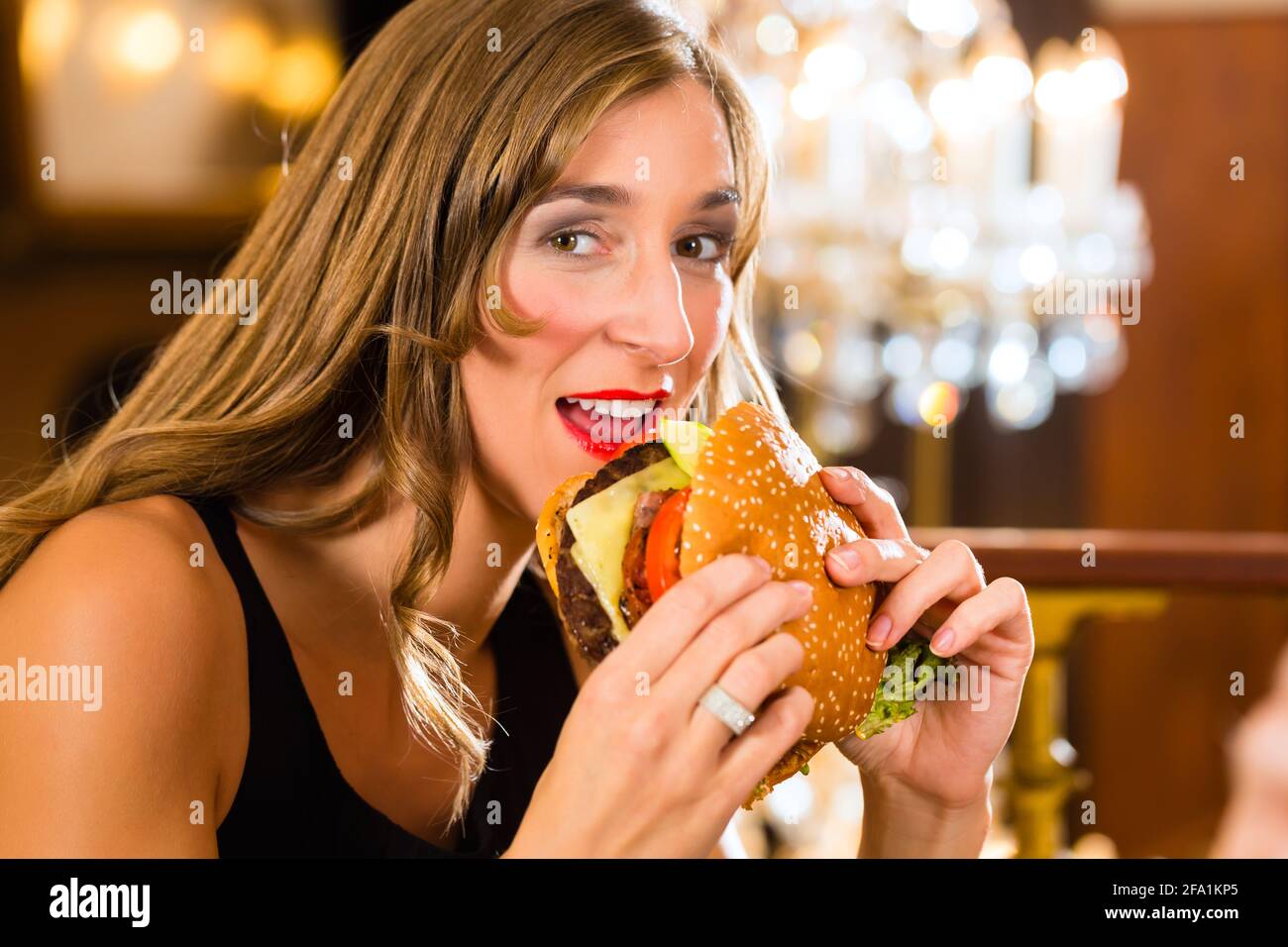 Junge Frau in ein feines Restaurant Essen, einen Hamburger, sie verhält sich nicht ordnungsgemäß Stockfoto