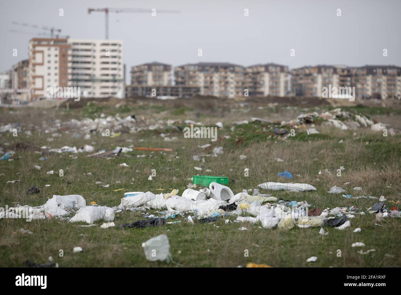 Bucharest, Romania - April 2, 2021: Piles of industrial and home waste lay on a field near inhabited blovks of flats. Stockfoto