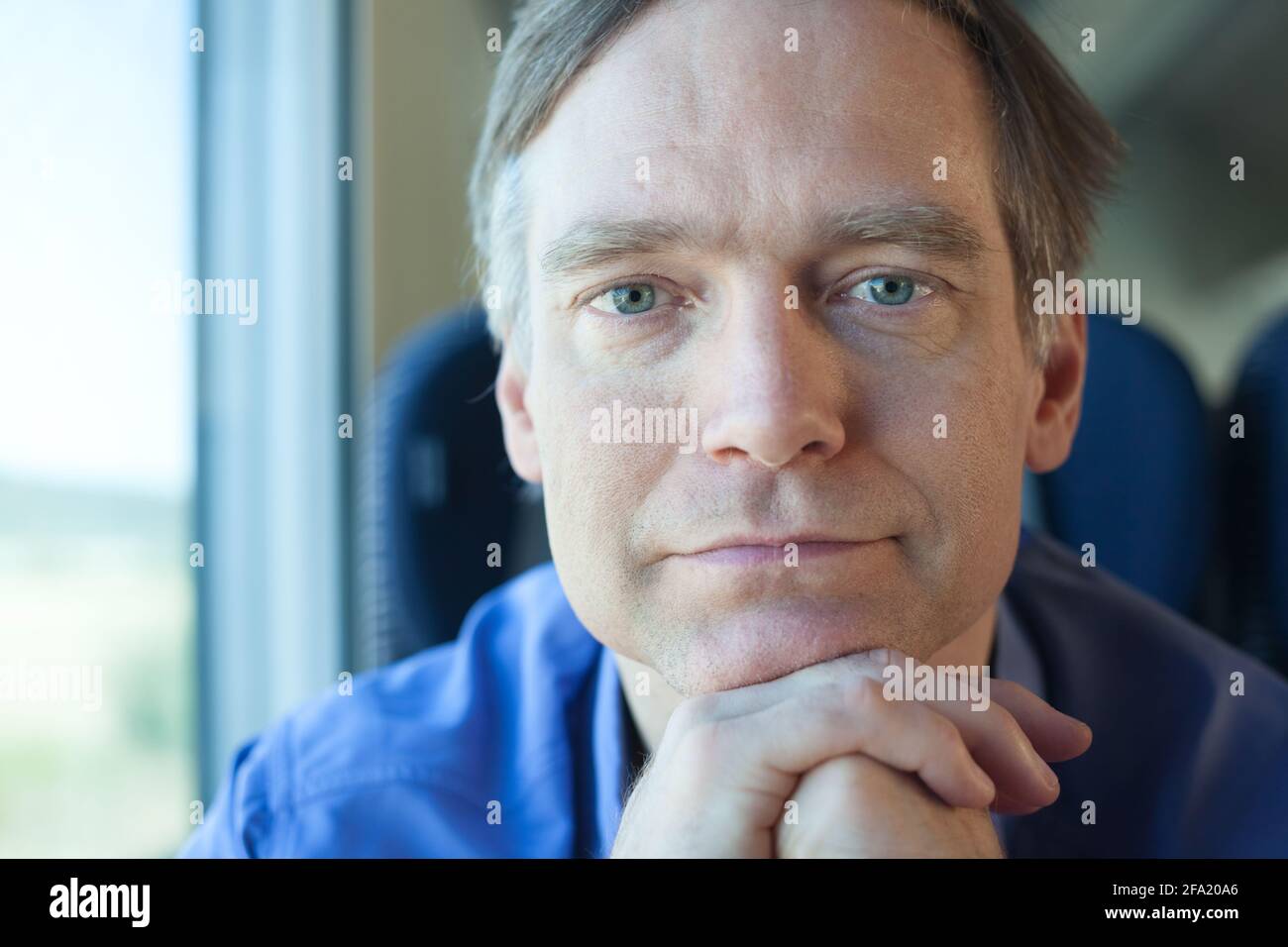 Kaukasischer Mann im Zug lehnte sich vorwärts Kinn auf der Hand mit Nachdenkliches Lächeln beim Blick auf die Kamera Stockfoto
