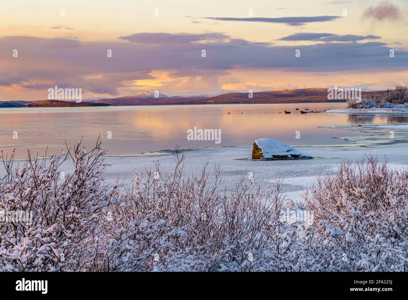 Winterlandschaft bei Sonnenuntergang mit buntem Himmel und Wolken, offenem Wasser und Farben, die sich im Wasser spiegeln, Schwedisch Lappland, Schweden Stockfoto