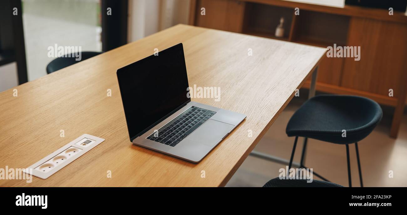 Laptop mit leerem Bildschirm auf dem Tisch und leerem Stuhl. Leerer Tagungsraum mit offenem Laptop und Stuhl neben dem Tisch. Stockfoto