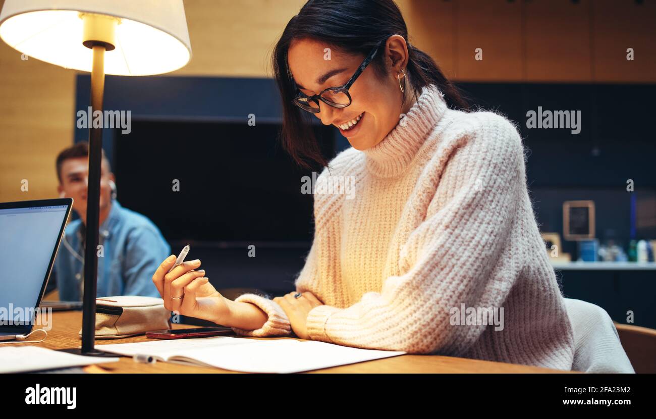 Mädchen lächelt, während sie ihre Studien in der Bibliothek. Junge Studentin in der Bibliothek sieht glücklich aus, während sie spät in der Nacht an der Universität studiert. Stockfoto