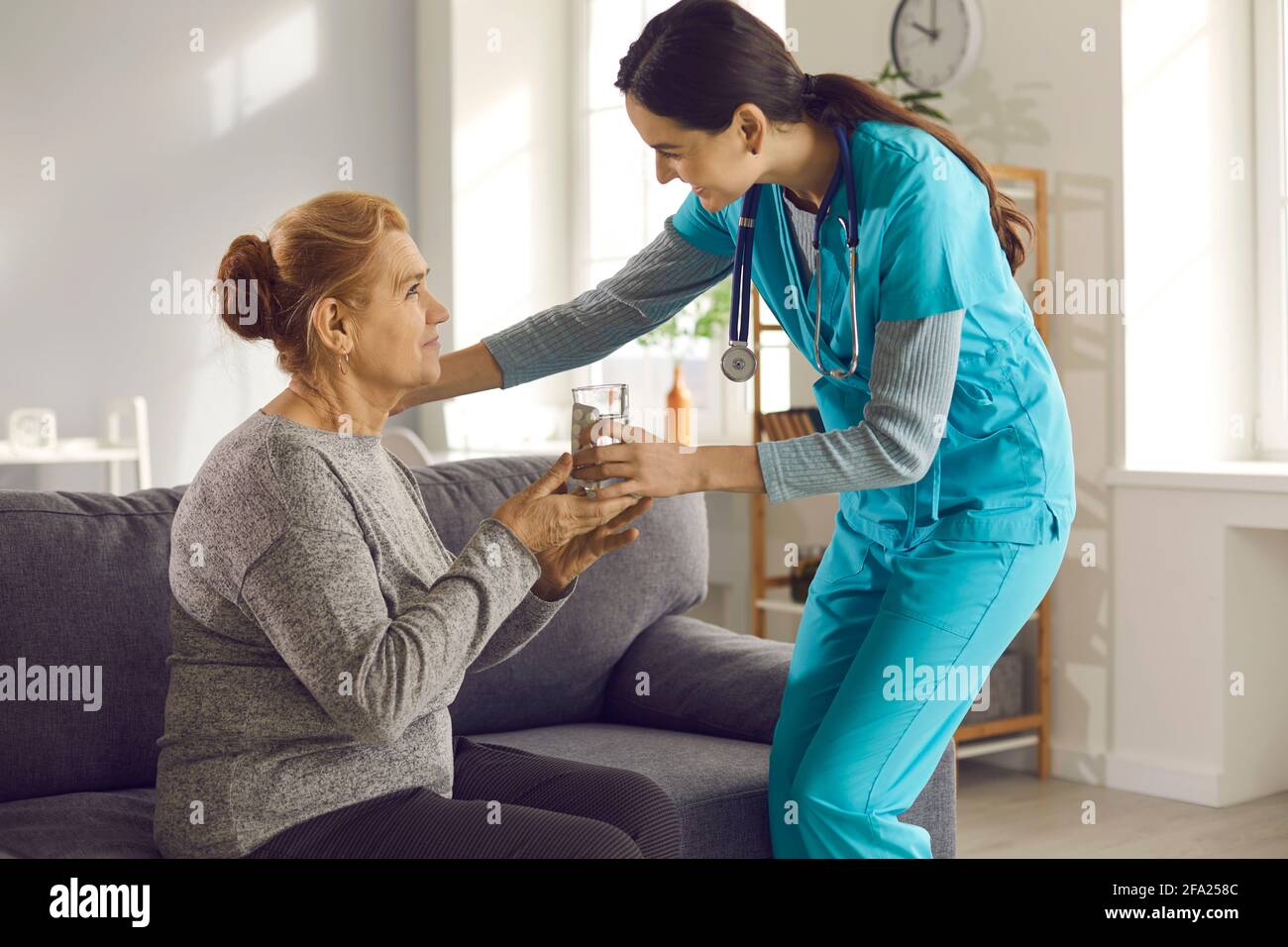 Krankenschwester, die zu Hause, in der Klinik oder in einer betreuten Einrichtung ein Glas Wasser an ältere Frauen gibt Stockfoto