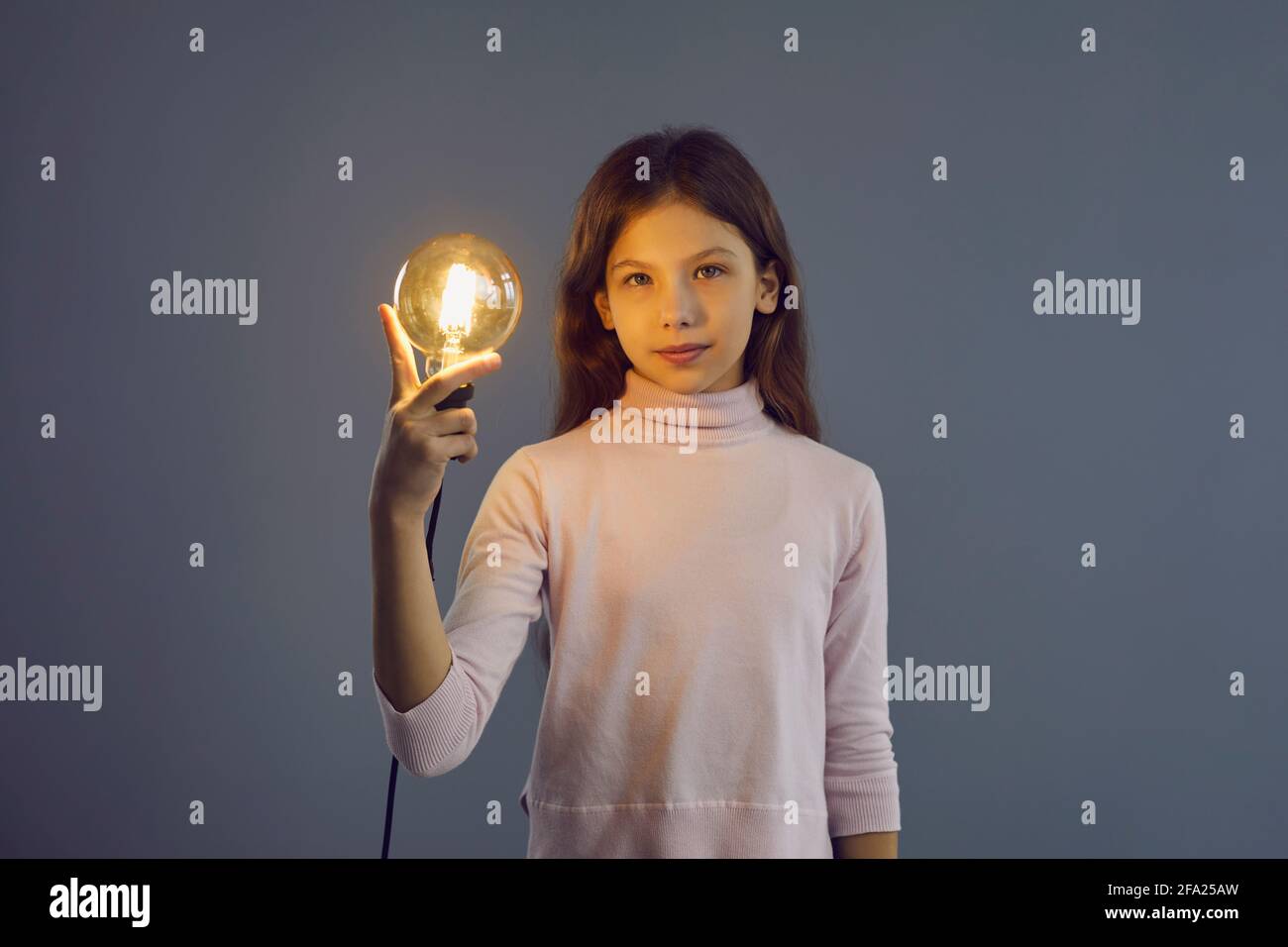 Smart intelligente Pre-teen Schulmädchen hält Idee Lampe Studio angeschossen Graue Wand Stockfoto