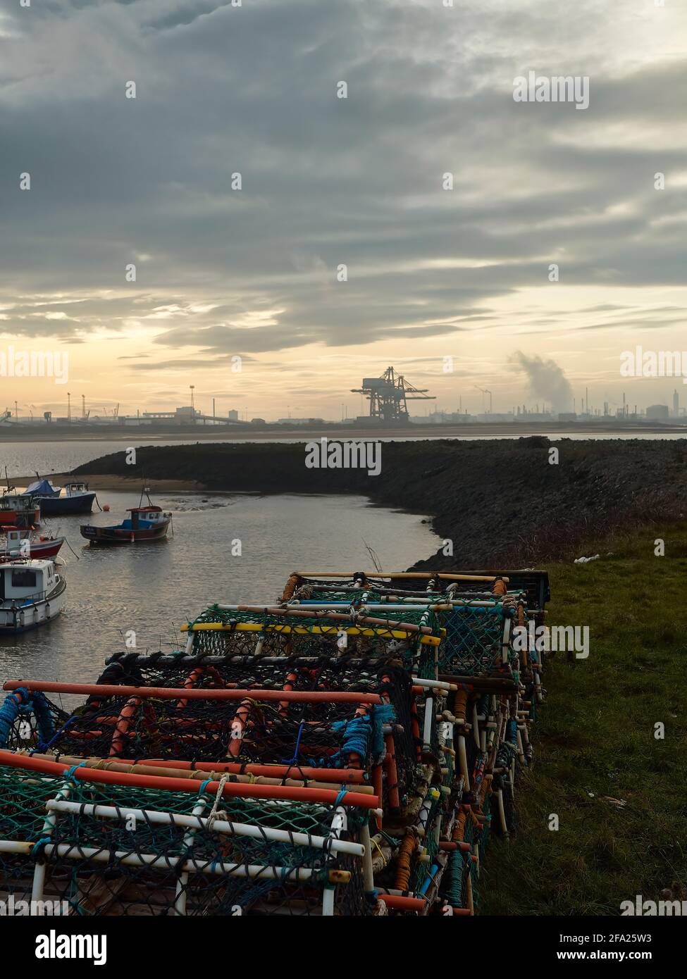Ein Blick über Paddy’s Hole, South Gare, mit Blick auf die kleinen Boote der Fischereiflotte und die Mega-Strukturen der Containerhäfen am Horizont. Stockfoto
