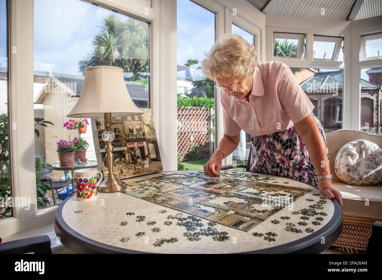 Eine ältere Frau in den Siebzigern, die in ihrem Wohnsitz, England, ein Puzzle macht Stockfoto