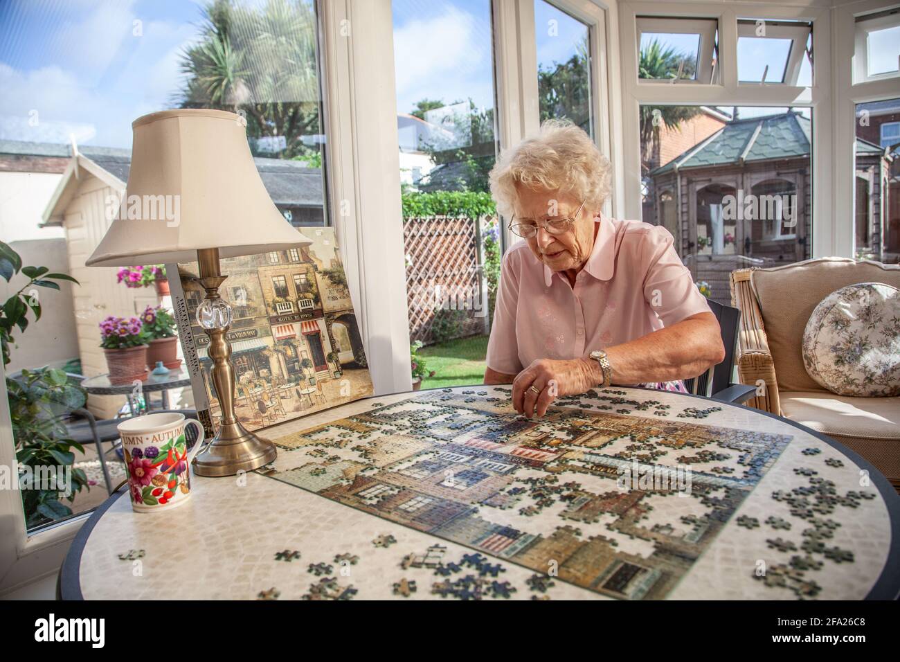 Eine ältere Frau in den Siebzigern, die in ihrem Wohnsitz, England, ein Puzzle macht Stockfoto