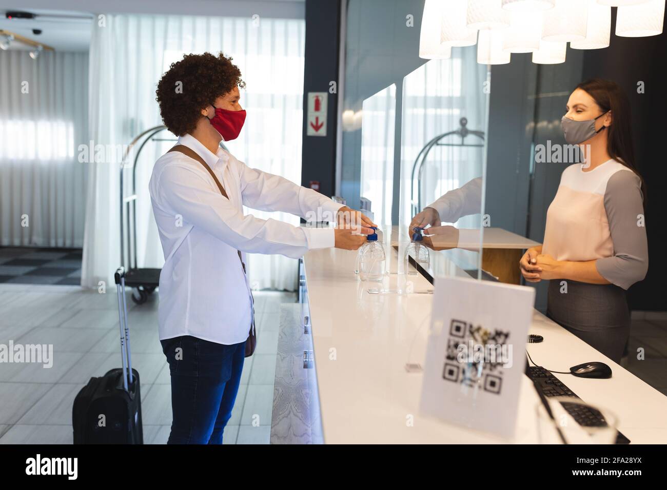 Ein vielseitiger Geschäftsmann mit Gesichtsmaske, der die Hände desinfiziert und mit dem Rezeptionisten spricht Im Hotel Stockfoto